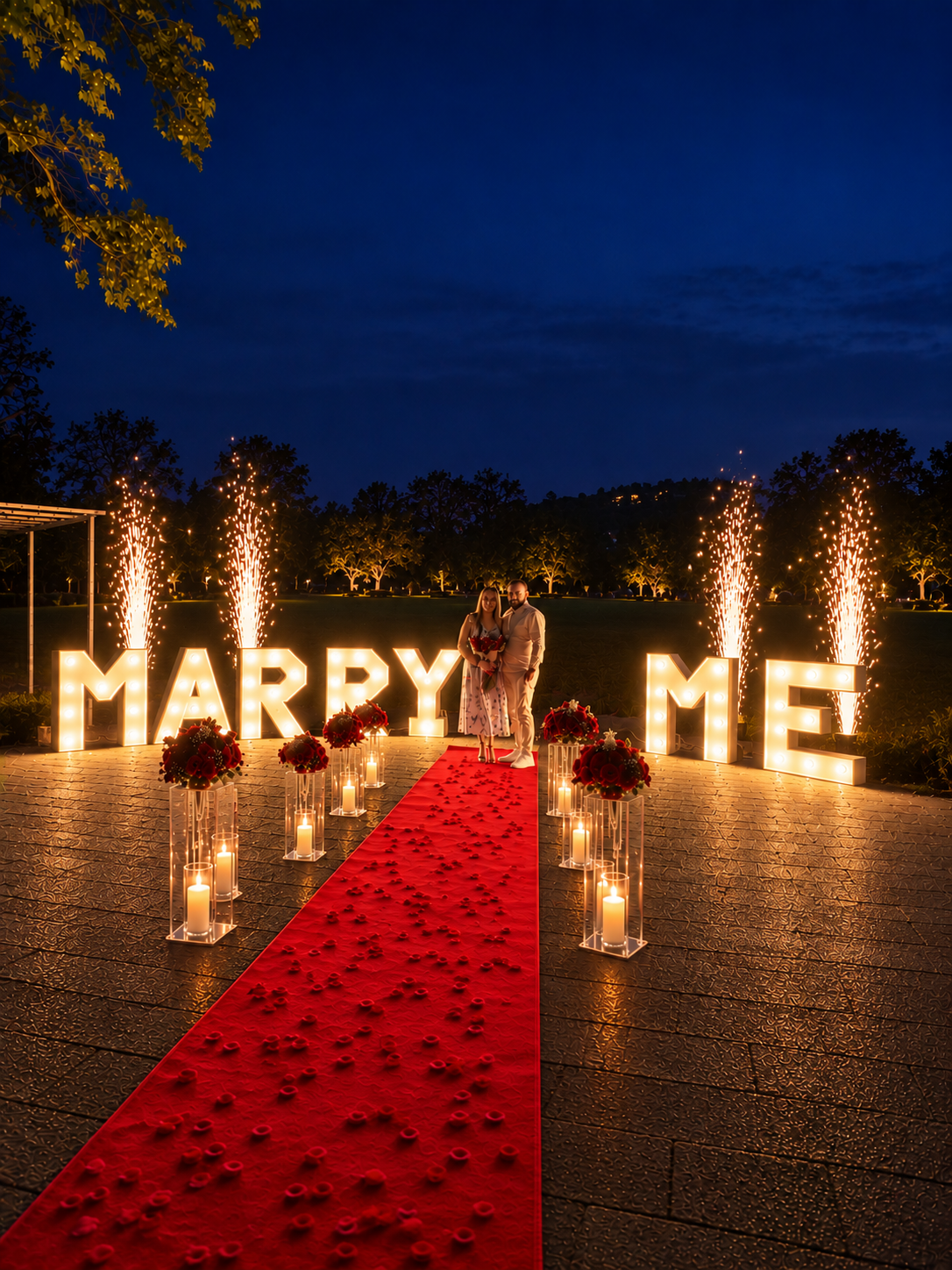 Paar vor leuchtenden Marry-Me-Buchstaben, Fontänen und rotem Teppich bei Nacht